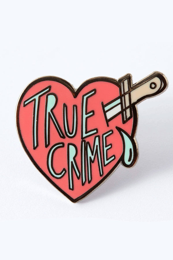 Enamel pin of a pink heart that is being stabbed by a knife. The pin says True crime with a tear drop next to it.