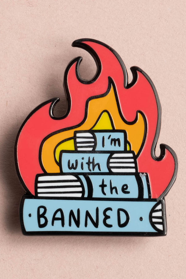 Enamel pin that features a stack of 4 books in front of a fire. The pin says I;'m with the banned on the spines of the books.