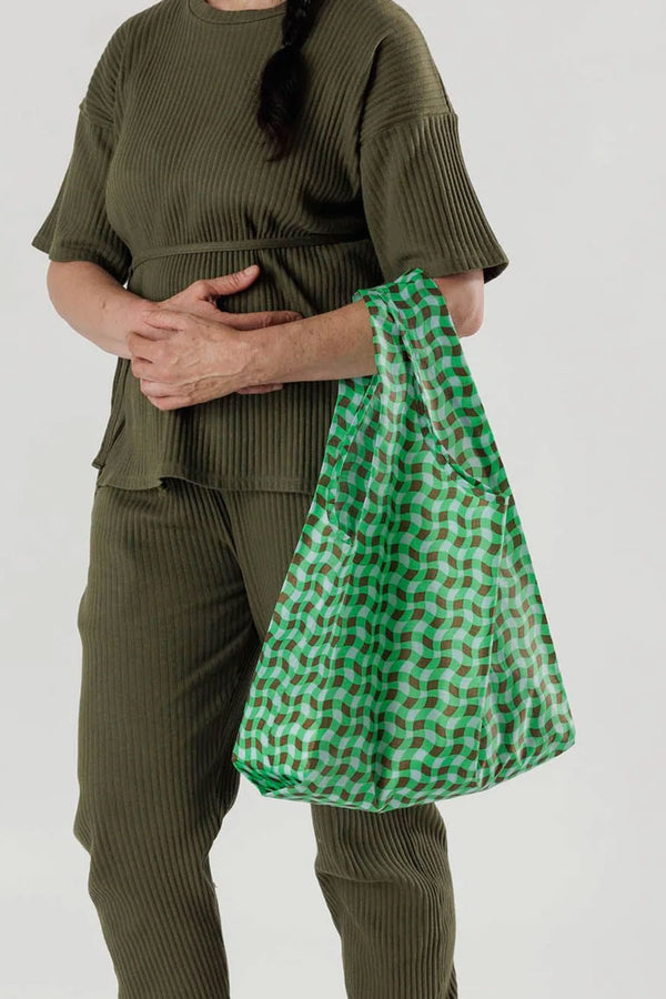 A person holding a Wavy green and brown gingham reusable tote. White background.