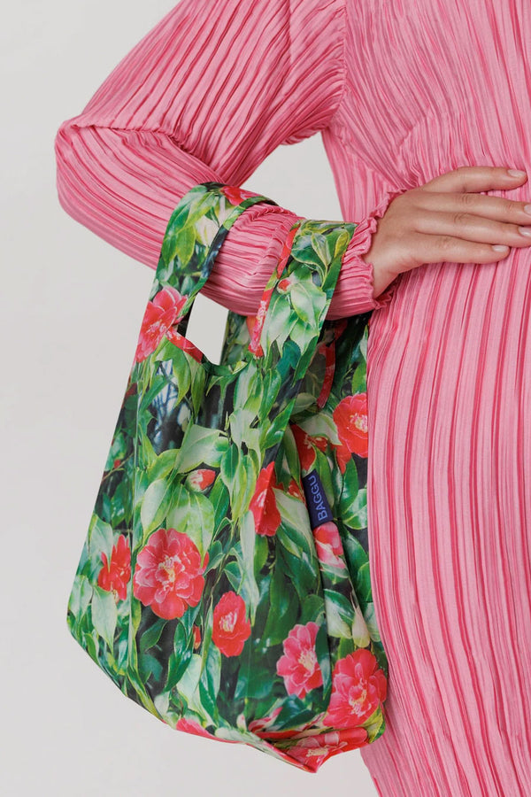 A person holding a Reusable shopping bag covered with a photo of red flowers and leaves all over it. White background.