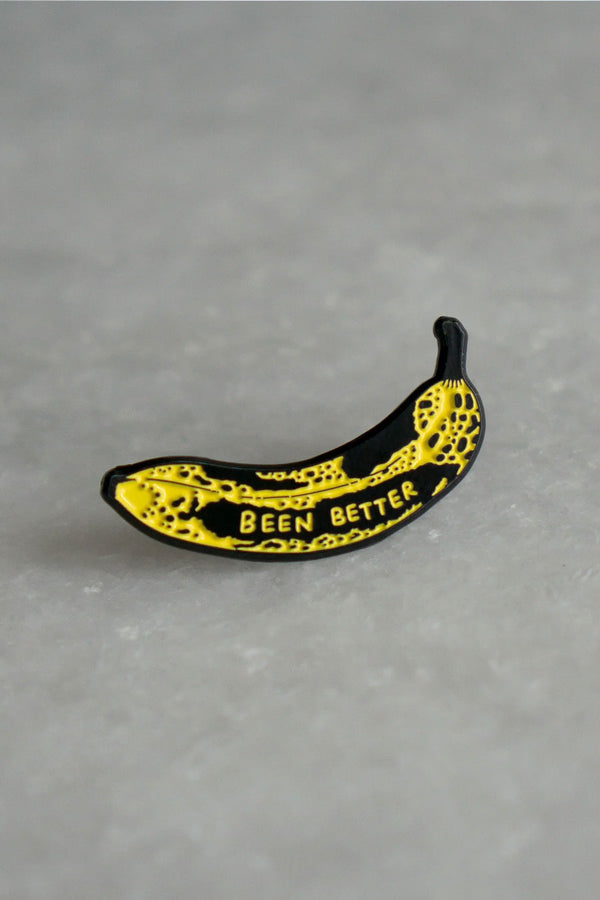 Yellow Bruised banana enamel pin. On top of a bruise, the pin says Been Better in yellow text. White Marble background.