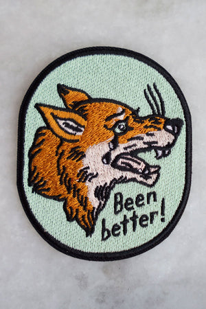 Mint green oval patch with black border. The patch features a crying orange wolf that is crying. Below that the patch says Been Better in black text. White marble. 