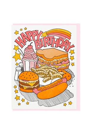 greeting card of a pile of fast food. Shake, sandwich, fries, burger, and hotdog. Above the food is a shooting star with a yellow, orange, and pink rainbow trailing behind. The card says Happy Birthday. Pink envelope. White background.