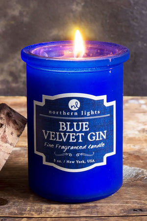 Blue glass candle jar with a raw edge cork top. Candle has a blue label that says Blue Velvet Gin. Natural wood backdrop.