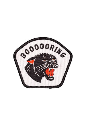 White embroidered patch with black edge. The patch features a black panther head with its mouth open showing its teeth. Above the panther the patch says "Boooooring" in black lettering. White background.