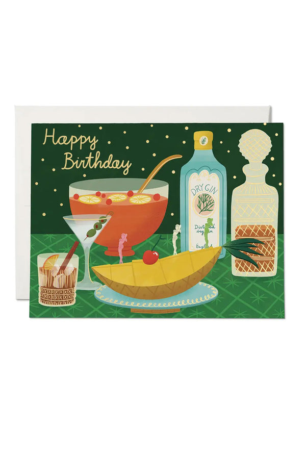 Green greeting card featuring an illustration of a punch bowl, bottle of gin, decanter, highball and martini glasses, and a slice of pineapple on a dish with a cherry on top. The card says Happy Birthday in yellow lettering. White background.
