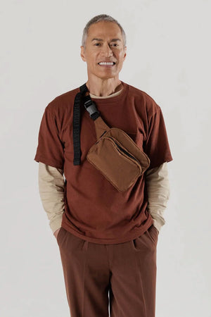 A person wearing a Brown fanny pack with two compartments and black nylon straps across their chest.