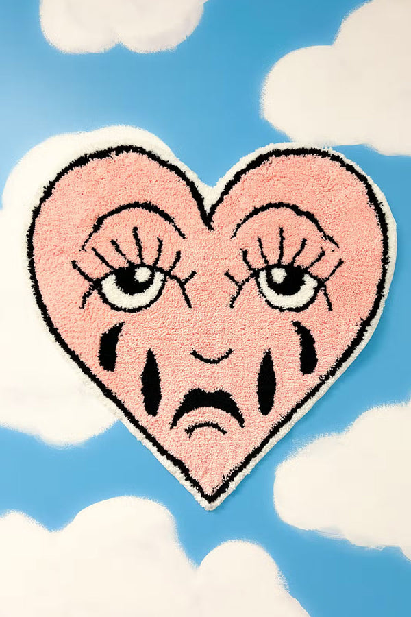 Heart shaped floor rug that features a crying face in traditional tattoo style. Blue sky background.