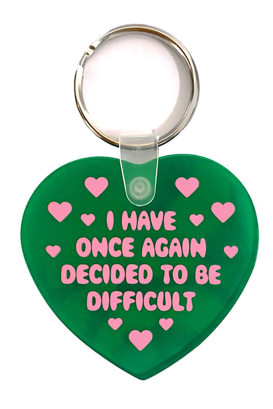 Green flexible heart shaped keychain. They heart says "I have once again decided to be difficult" in pink text. Surrounding the text are small pink hearts.