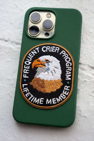 Oval shaped embroidered patch featuring a crying Eagle surrounded by text that says Frequent Crier Program. Lifetime Member. Patch is adhered to a green cell phone case.