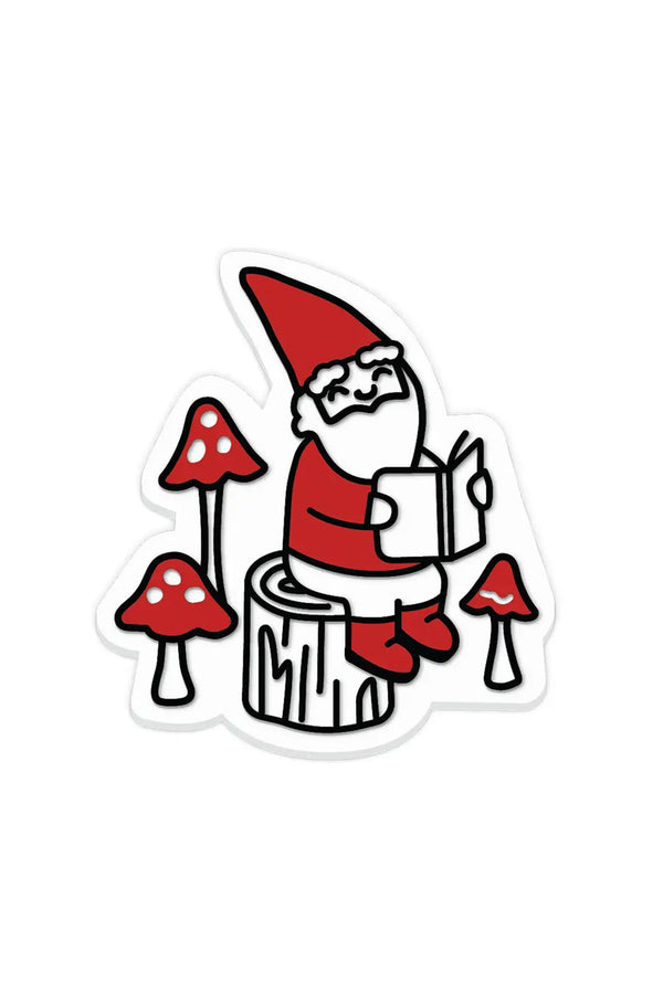 Magnet of a gnome sitting on a tree stump with a book surrounded by mushrooms.