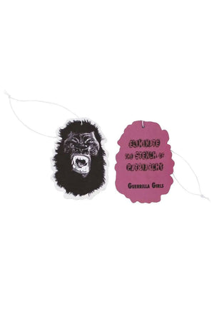 Air freshener of a Gorilla Face. The back of the air freshener, is pink and says Eliminate the stench of the patriarchy. Guerrilla Girls. White background.