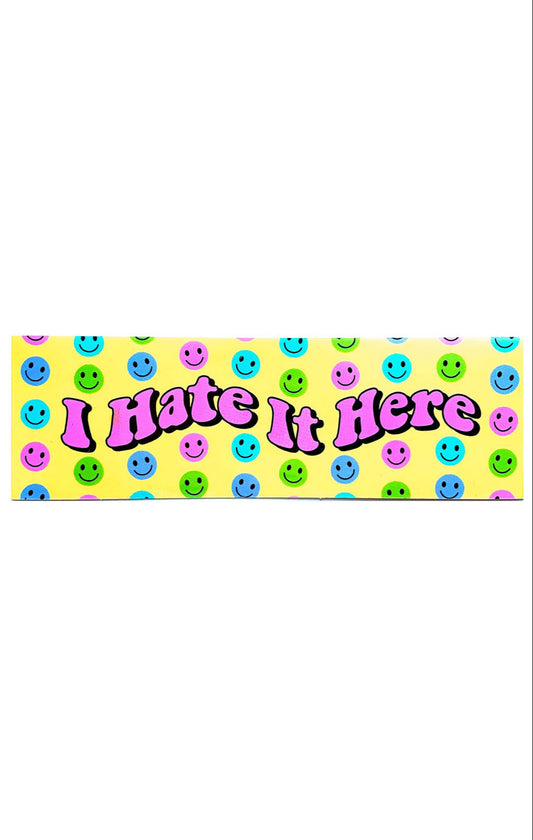 Yellow vinyl sticker that says I Hate It Here in pink bubble letters. Smiley faces in blue, aqua, green, and pink surround the lettering.