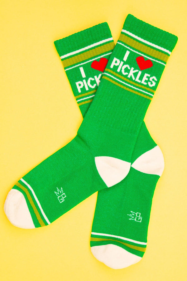 One pair of green mid calf athletic socks with a white heel and toe. Light green and and white stripes run across the toes and around the top of the socks. In white lettering the socks say I Heart Pickles.Yellow background.