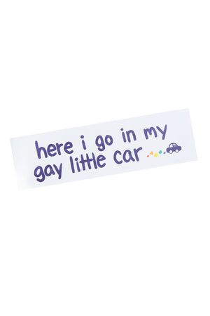 Bumper sticker that says 'here i go in my gay little car' with a purple little card with rainbow hearts behind it.
