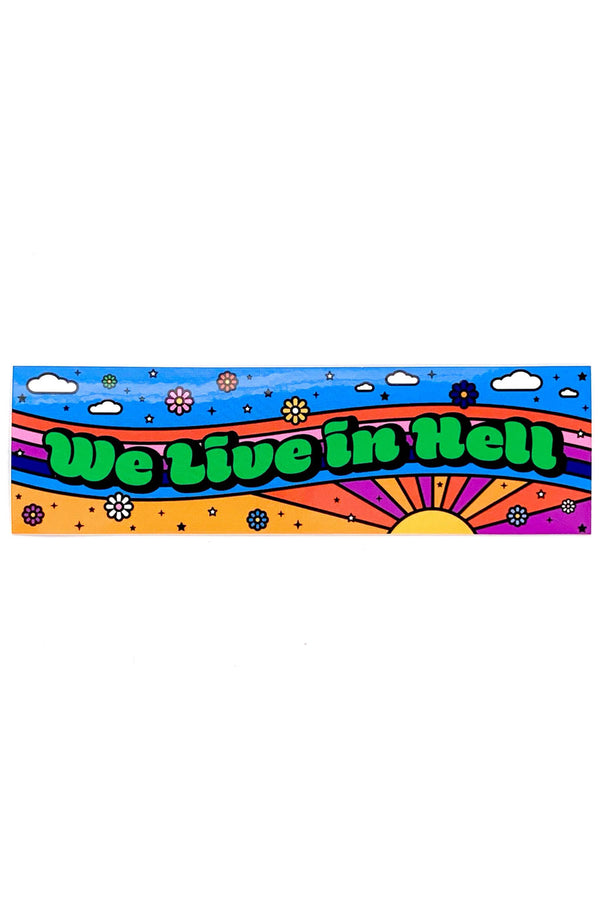 Vinyl sticker that says We Live in Hell in green lettering. The sticker features a blue sky at the top, red, pink, and blue stripes beneath that. And a sunburst with yellow pink and orange rays at the bottom of the sticker.
