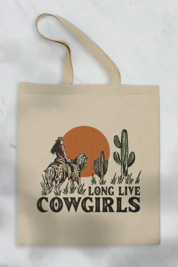 Natural cotton tote featuring a cowgirl on a horse standing next to cacti in front of a large sun. Under the illustration in black western style text the tote says Long Live Cowgirls. White background.