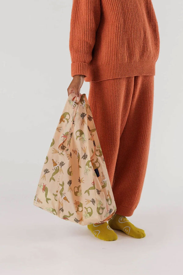 A person holding a Light pink reusable tote featuring illustrations of Mermaid Bunnies and Carrot bundles printed all over it.
