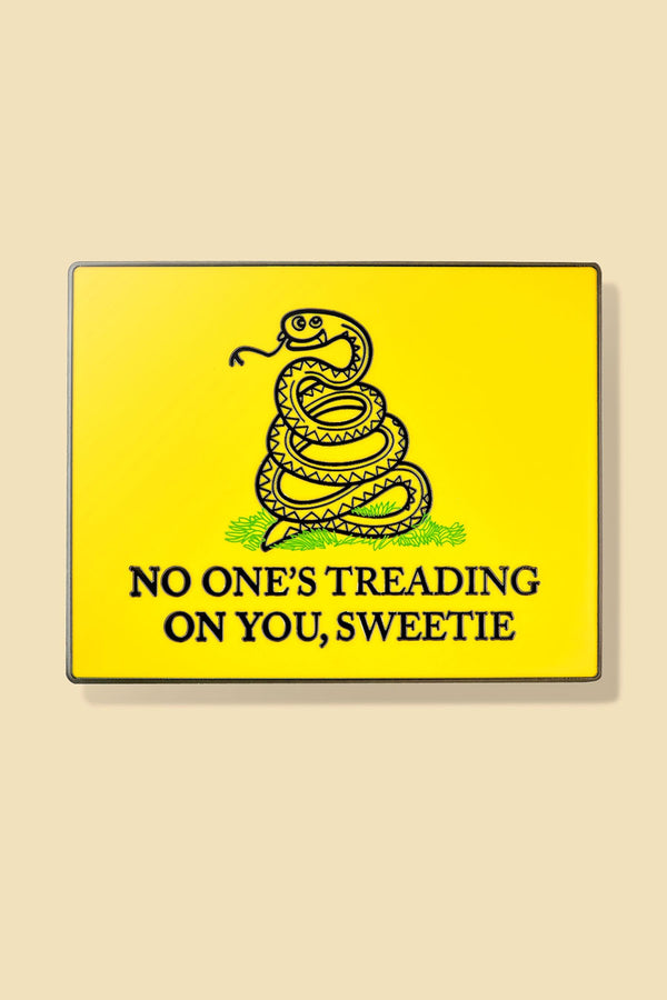 Enamel pin of a parody design of a snake on a yellow background. Under the coiled snake the pin says, No One's Treading on you , Sweetie.