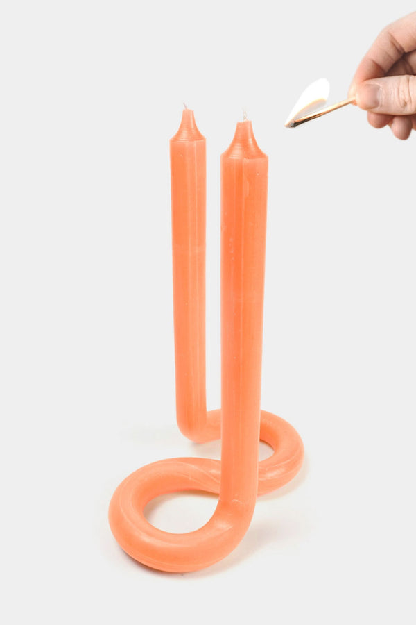 Someone lighting an orange twist candle with two wicks.