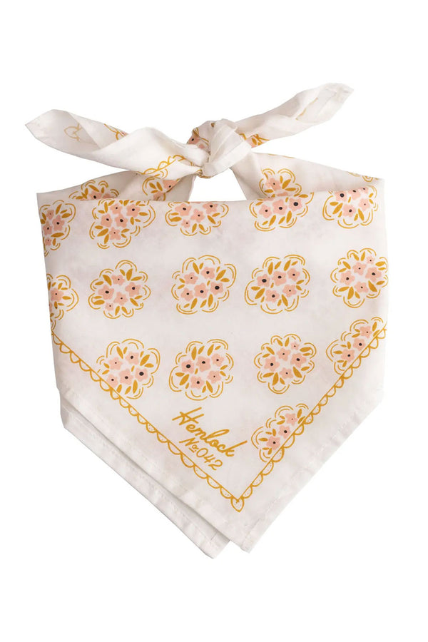 A knotted White bandana featuring dainty clusters of pink flowers printed all over with a scallop line work border. White background.