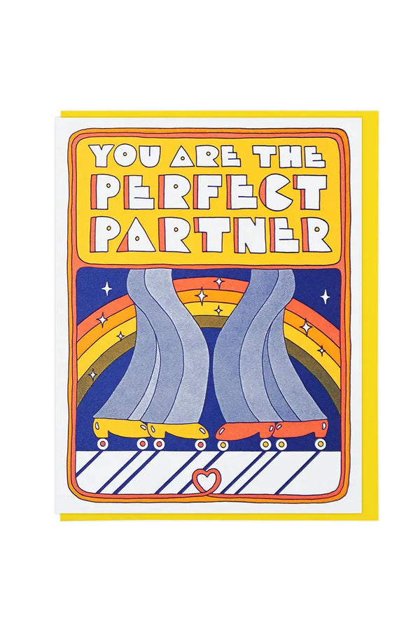 Greeting card of two roller skaters face to face. The Illustration is of their legs and skates in front of a rainbow. Above them, the card says You are the Perfect Partner in block letters. Yellow envelope. White background.