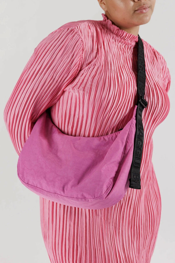Woman with a Pink nylon crescent shaped cross body bag with black straps.
