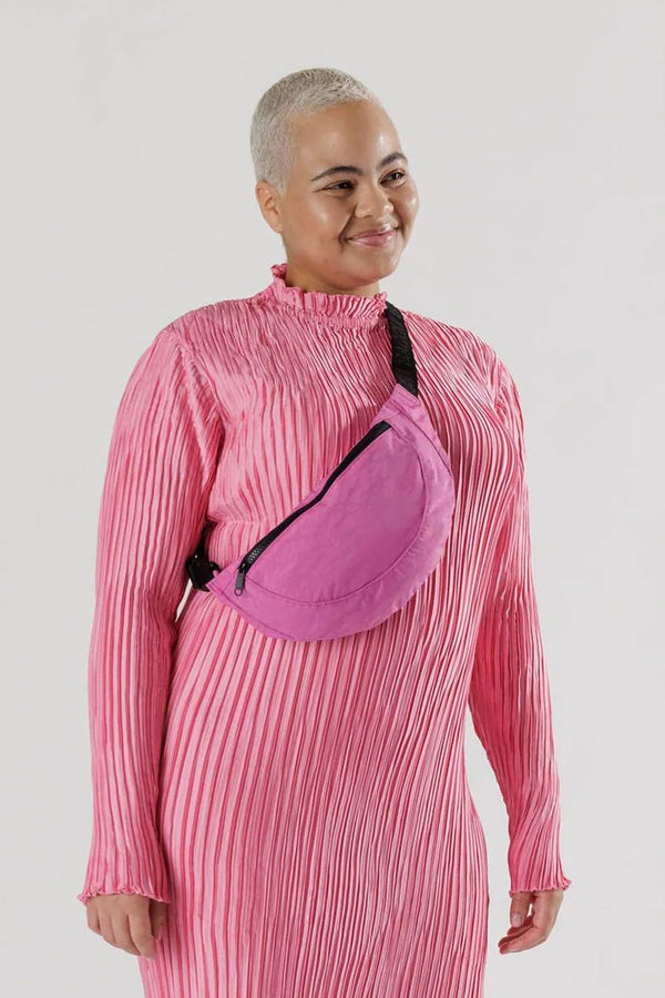 Woman wearing a pink nylon fanny pack with black strapsacross her chest.