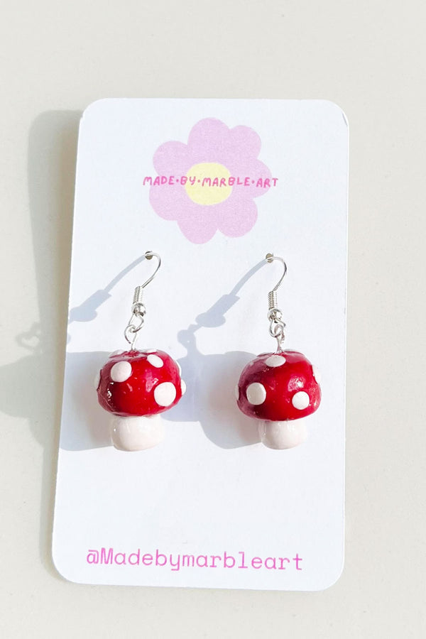 Handmade red and white polymer clay mushroom earrings. The mushrooms are attached to dangly earrings with silver jump ring.