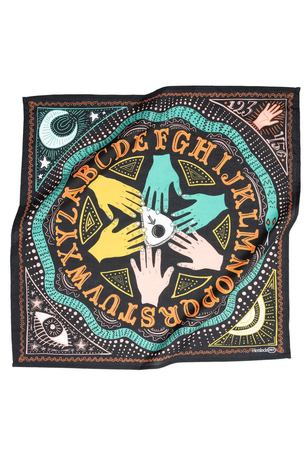 Black bandana featuring an illustrated ouija board scene. Each corner hosts a different element: Moon, Sun, Eye, Palm of hand. The illustration is orange, yellow, teal, and pink. White background.