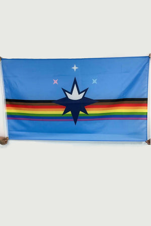 Two people holding pride version of the Springfield City flag. This flag features a rainbow stripe with brown and black stripes added to it. On top of the stripes is one big star with a crown and three small stars above that. White background.