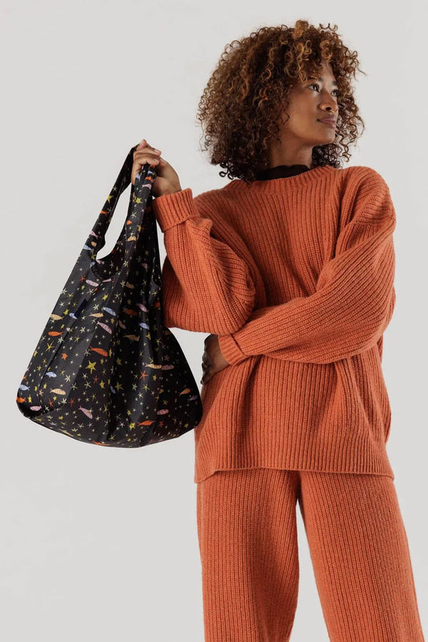 Person holding standard sized reusable black tote bag which features multicolor fish and stars all over it.