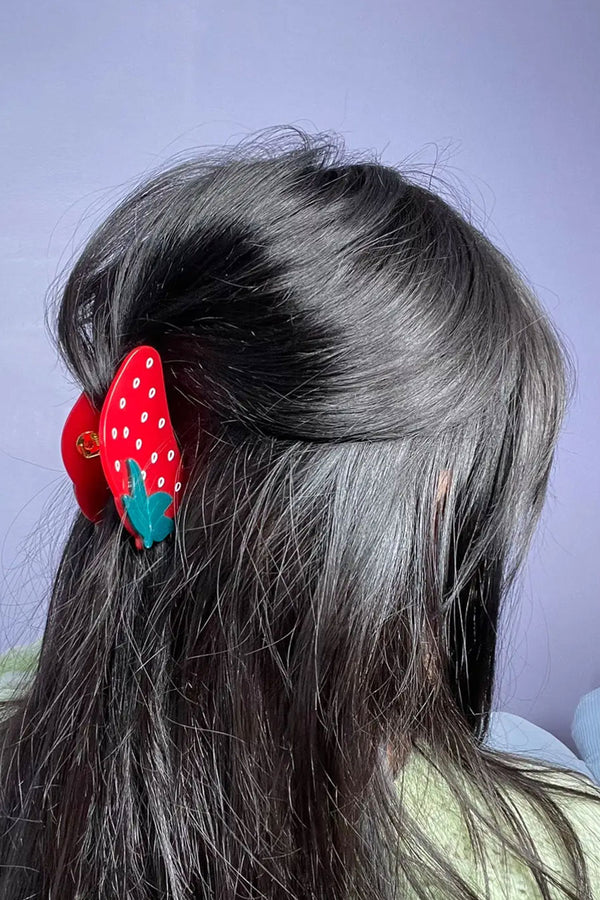 A person wearing their hair up held by red plastic strawberry hairclip. Blue background.