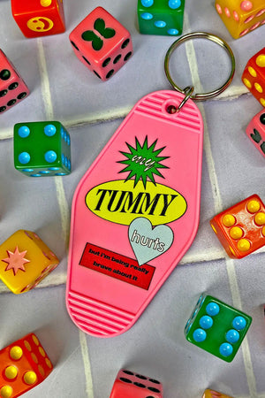 vintage motel style keychain. The keychain is pink and says My Tummy Hurts but I'm being really brave about it. Behind the text is a green starburst, yellow oval shape, a blue heart, and a red rectangle.