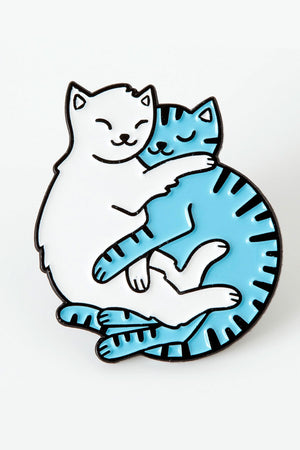 Enamel pin of two cats cuddling with each other. One cat is white, the other cat is blue with black stripes.