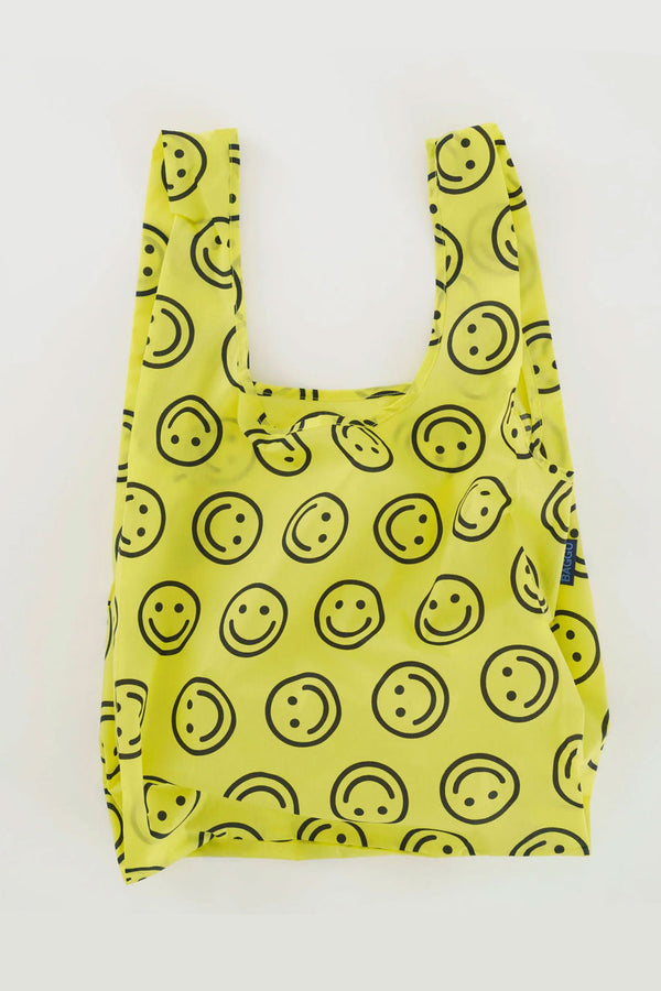Yellow reusable tote with black smiley faces printed all over. White background.