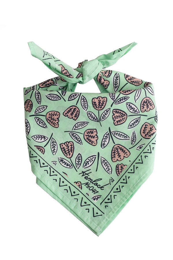 A mint green bandana with a pattern of whimsical pale pink flowers, folded and tied in a knot.