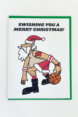 A white greeting card with an illustration of Santa Claus playing basketball. The text reads "Swishing you a Merry Christmas!"