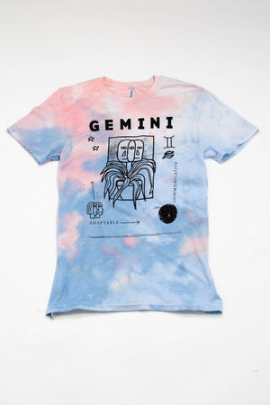A light blue and peach tie-dyed tee with illustrations and images depicting the zodiac sign "Gemini."