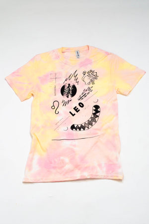 A yellow and pink tie-dyed t-shirt on a white background. The shirt has illustrated images of the sun, a lion, and the astrological symbols for the sign Leo.