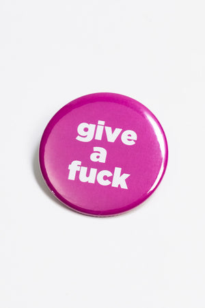 A hot pink pinback button with white text that reads "give a fuck."