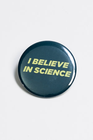 A dark green pinback button with the words "I believe in science" in yellow block lettering.