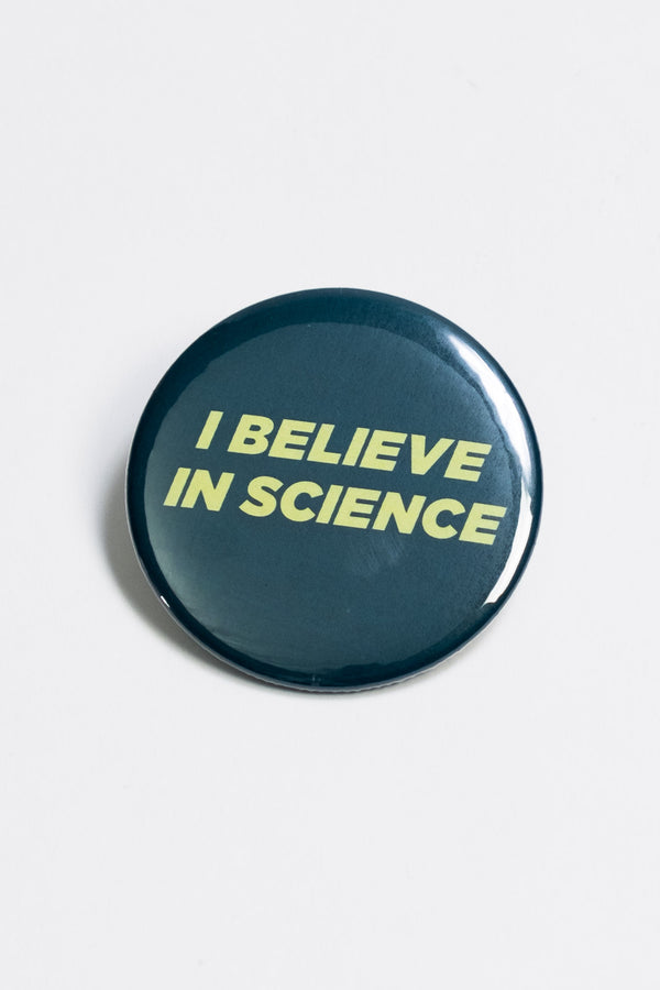 A dark green pinback button with the words "I believe in science" in yellow block lettering.