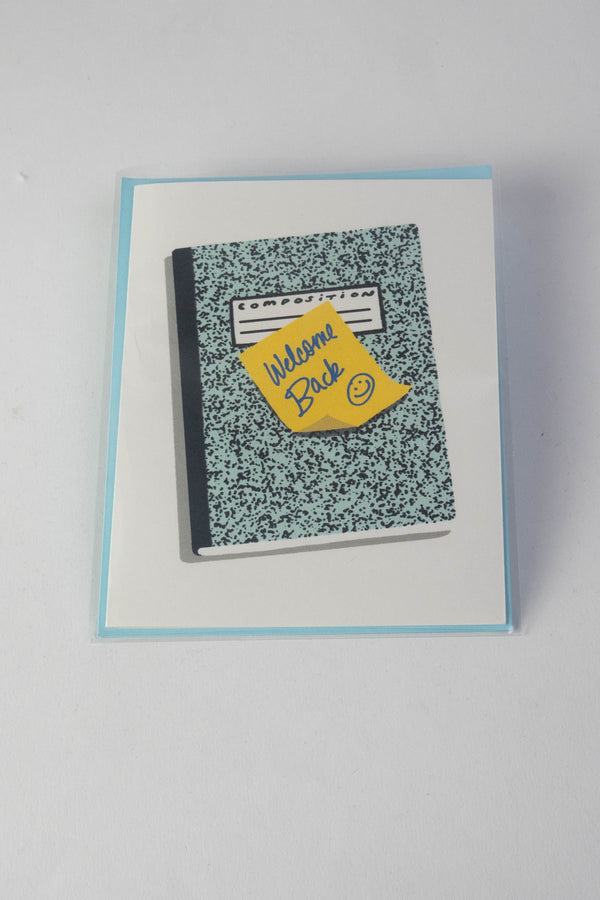 A white greeting card with an illustration of a blue and black composition notebook with a yellow post-it attached that reads "Welcome back" with a smiley face. 