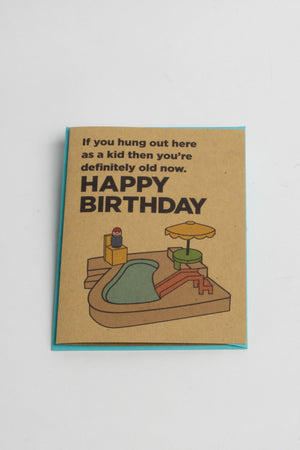 A kraft-paper greeting card with an illustration of a Fisher Price pool playset. The text reads "If you hung out here as a kid then you're definitely old now. Happy Birthday!"