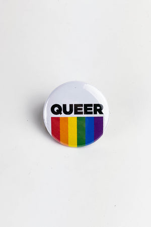 A round white pinback button with the word "Queer" in black block letters and lines of the rainbow flag below it. 