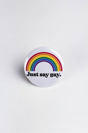 A white pinback button with a large colorful rainbow. The black text reads "Just say gay."