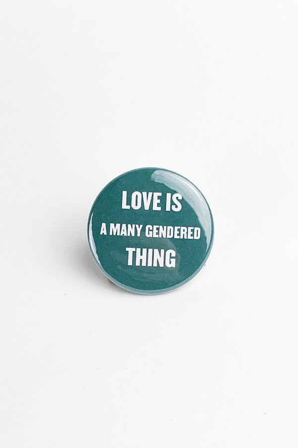 Blue Green Button on a white background that says " Love is a many gendered thing" in white text.