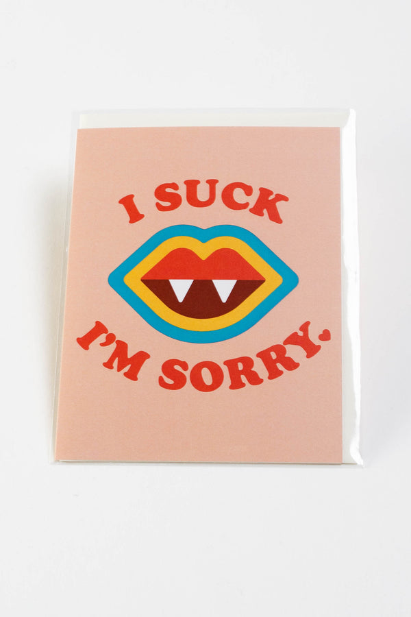 A peach colored greeting card with a blue, yellow, and red pair of lips with 2 white fangs. The text reads "I suck, I'm sorry."