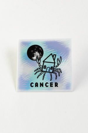 A square sticker with purple and blue coloring. The image is of a house with crab legs holding the moon in one of its claws. The astrological sign "Cancer" is written on the bottom.